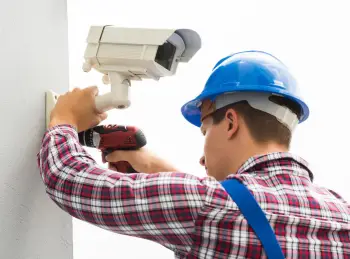 A white British man wearing a shirt of red & white checks and installing cctv