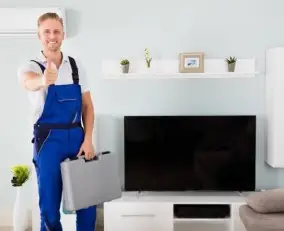 A British man wearing a white T-shirt, blue pants, stands with a tool kit in hand to repair TV